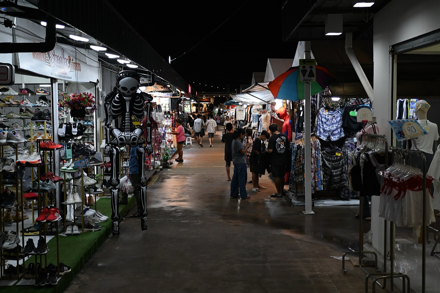 ทางเดินตลาดกลางคืนที่มีร้านเสื้อผ้าและรองเท้าเรียงราย